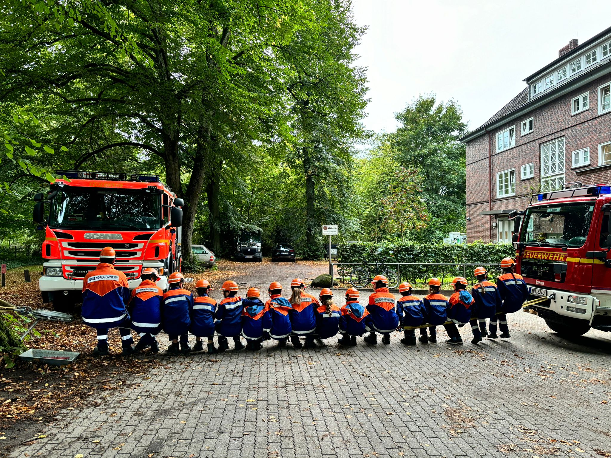 Mitglieder der Jugendfeuerwehr Ohlstedt sitzen zwischen den beiden Feuerwehrfahrzeugen vor dem Gerätehaus